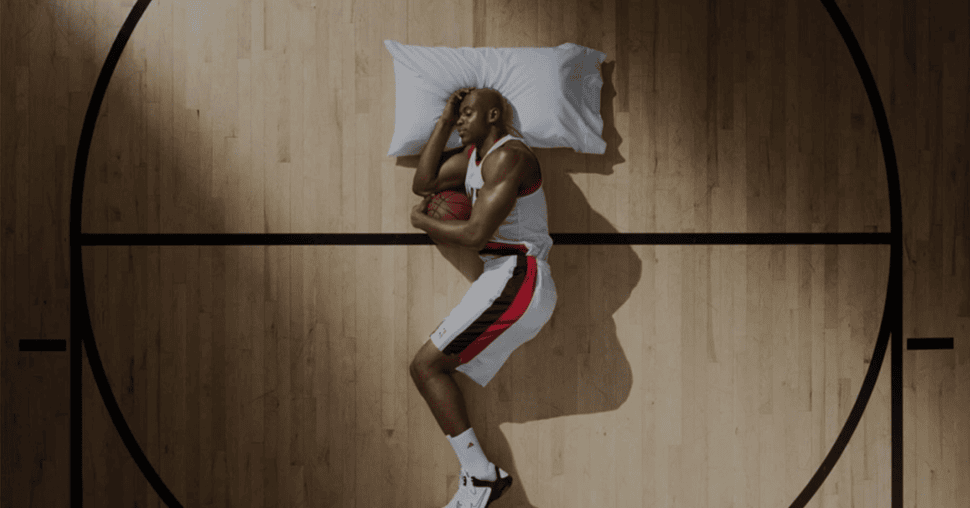 Basketball player lying asleep on a pillow in the centre circle of a court