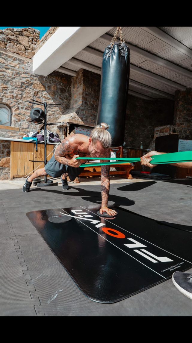 An athlete working through a resistance-band exercise on a gym mat beside a punchbag.