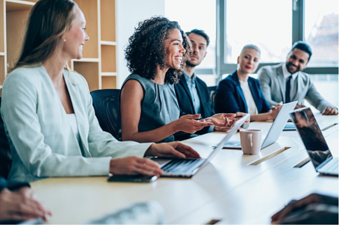 A group of colleagues sitting along a boardroom table with laptops during a meeting.