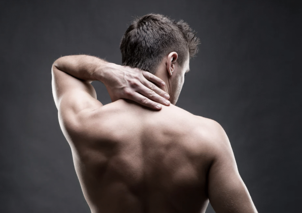 Man seen from behind reaching over his shoulder to hold the back of his neck