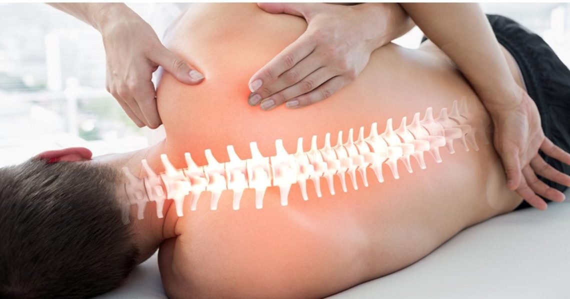 A therapist's hands treating a man's back on a treatment couch, with an illustrated spine highlighted along it.